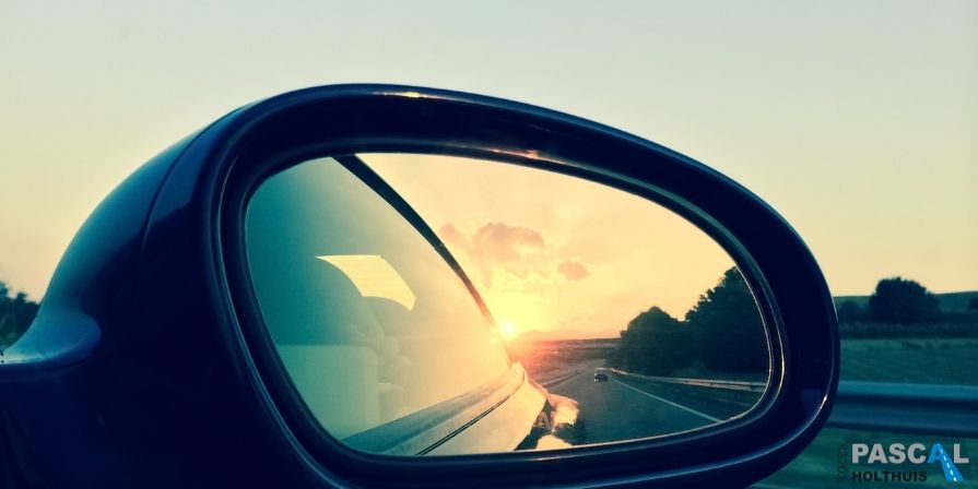 Zijspiegel van een auto met daarin de zon.