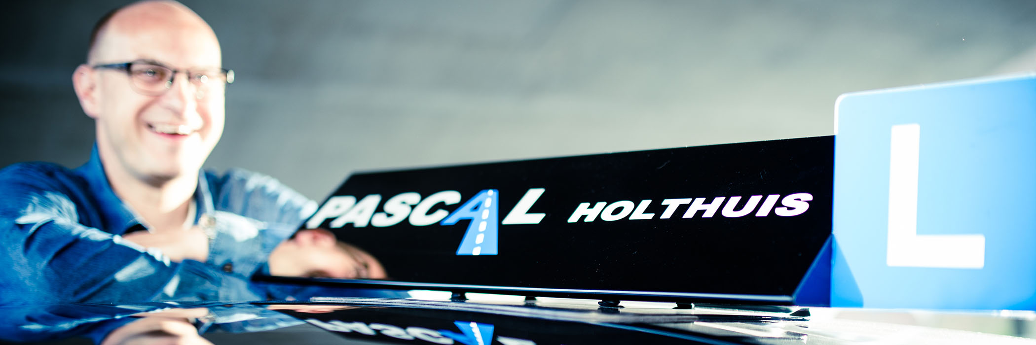 Pascal Holthuis naast zijn auto met het rijles bord
